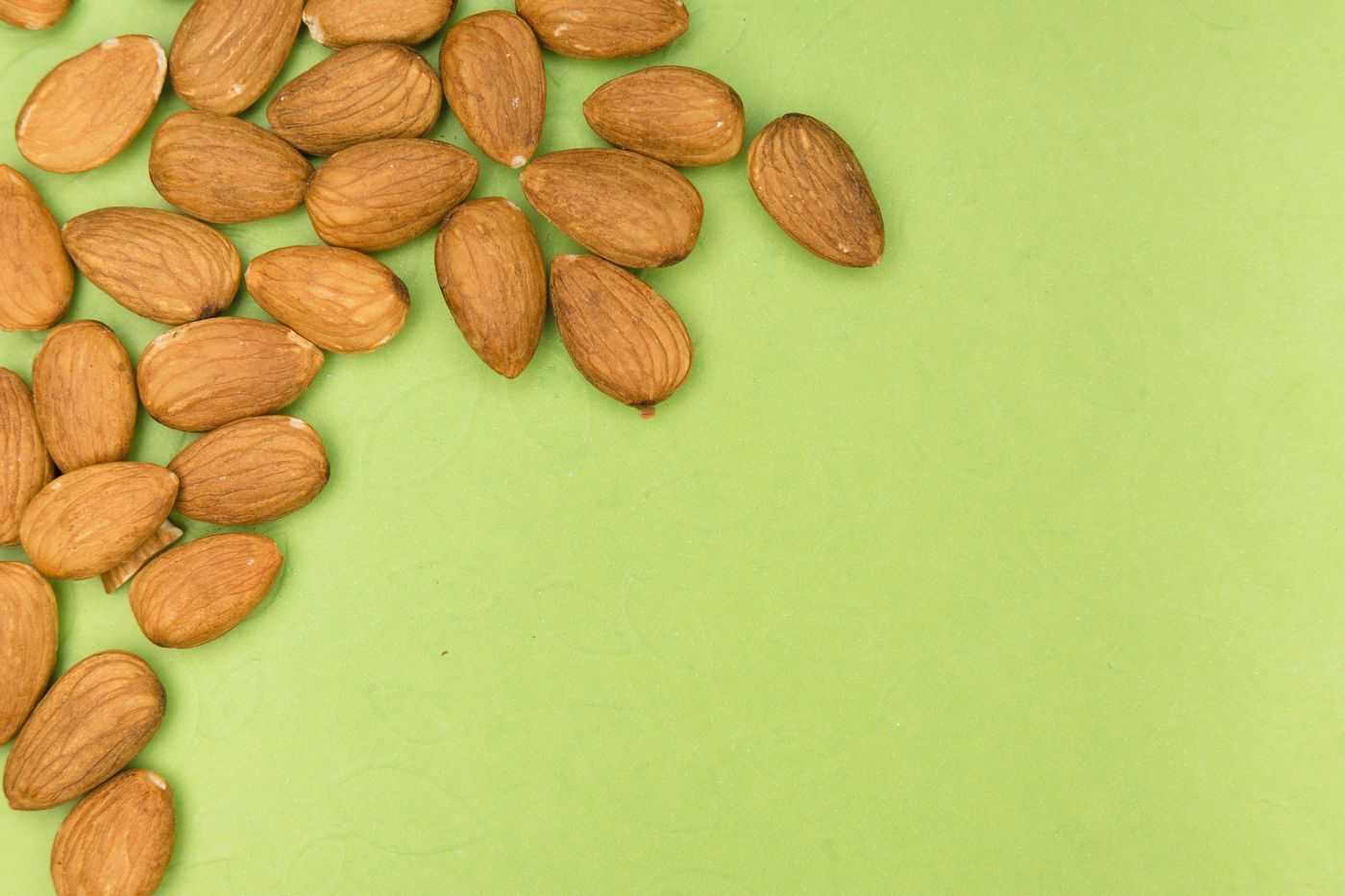 Almonds scattered across a bright green surface